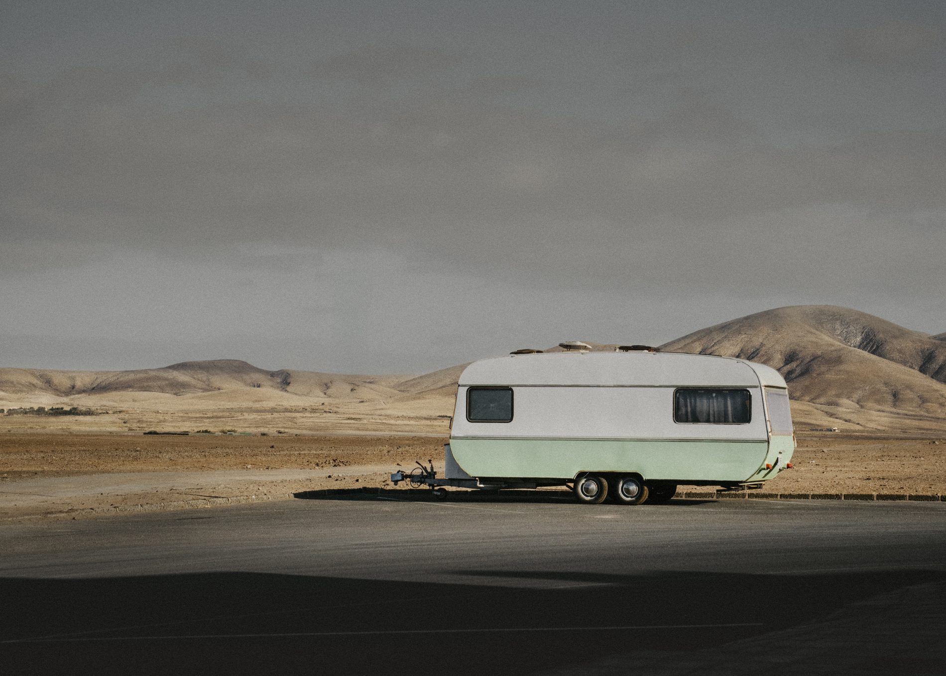 Caravana turquesa estacionada en paisaje desértico con montañas al fondo